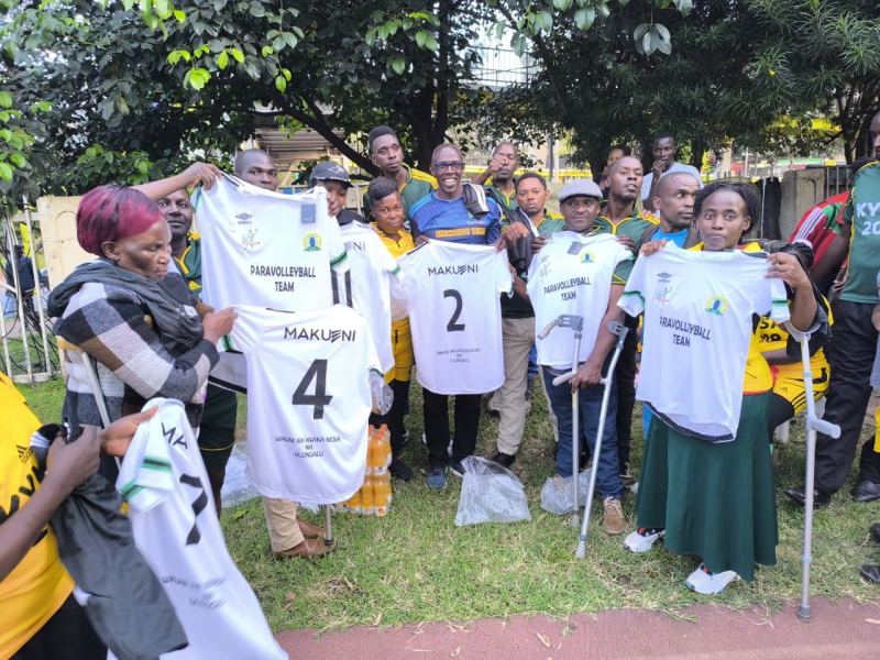 Makueni Para Volleyball team members, several on crutches, hold up their new county jerseys